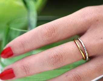 May include: Two thin gold and silver rings stacked on a finger. The rings have a hammered texture.