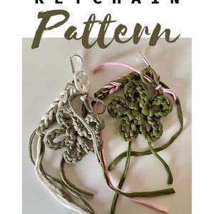 Può includere: Due portachiavi all'uncinetto fatti a mano. Uno è a forma di fiore in verde con accenti rosa, e l'altro è un design intrecciato in bianco e verde. Il testo "CROCHET KEYCHAIN Pattern" è in alto.