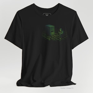 Puede incluir: Camiseta negra con un diseño verde de un hacker interactuando con un servidor. El diseño incluye un patrón de cuadrícula y líneas fluidas, con el texto "Hacker | Unisex Fit" en la parte inferior.