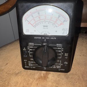 May include: A black Simpson Model 650 analog multimeter featuring a large white display with red and black scales, a central black rotary selector knob, and various input ports. The face is printed with CAUTION ON HIGH VOLTS and technical labels.