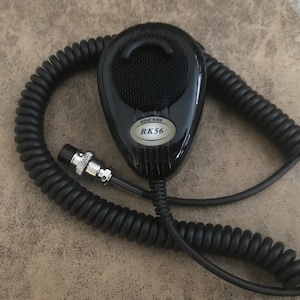 May include: A black microphone with a coiled cord and a silver label that reads "Road King RK56".