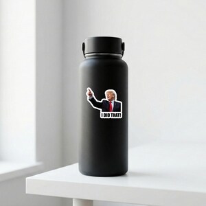 May include: A black insulated water bottle with a sticker of a man pointing and the words "I DID THAT!" The sticker features a man in a suit and tie. The bottle is on a white surface.