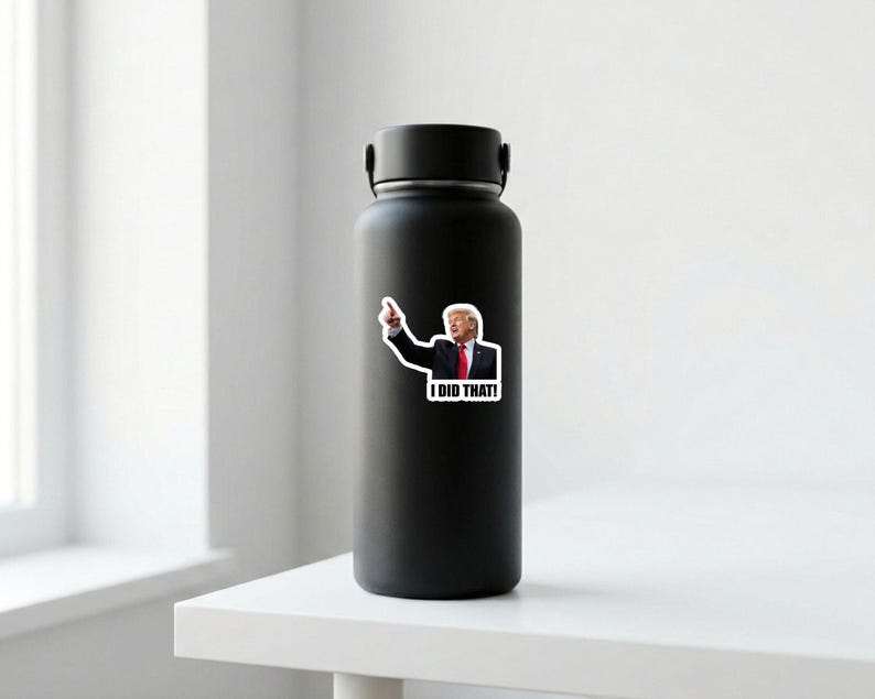 May include: A black insulated water bottle with a sticker of a man pointing and the words "I DID THAT!" The sticker features a man in a suit and tie. The bottle is on a white surface.