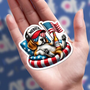 May include: A sticker featuring a cartoon beagle wearing sunglasses and a hat that says 'Merica'. The dog is relaxing on a red, white, and blue inflatable ring, holding a beer and an American flag.