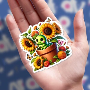 May include: A colorful sticker featuring a cartoon caterpillar in a flower pot surrounded by sunflowers, orange flowers, and butterflies. The caterpillar is green with big eyes. The sticker has a white border.