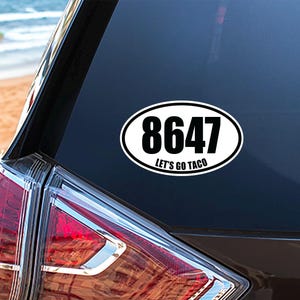 May include: Oval sticker with the number "8647" in bold black font, and the words "Let's Go Taco" in smaller black font, on a white background. The sticker is affixed to the rear window of a vehicle.