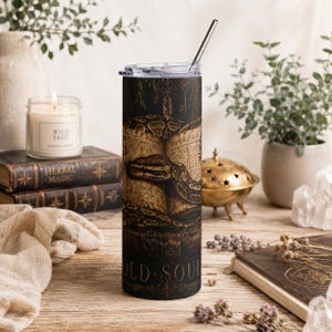 May include: A black and brown stainless steel tumbler with a snake and antique book design. The tumbler has a silver straw and a clear lid. The words "OLD SOUL" are printed on the bottom of the tumbler.