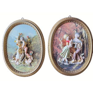 May include: Two oval wall plaques with gold frames. One shows a couple embracing, the other depicts two children with a rabbit. The plaques have a relief design with pastel colours and are set against a landscape background.