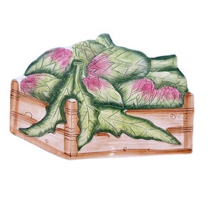 Puede incluir: Una fuente de cerámica con forma de caja de madera, llena de alcachofas. Las alcachofas son verdes con puntas rosas, y la caja está pintada en tonos marrones. El plato tiene un diseño rústico, ideal para servir.