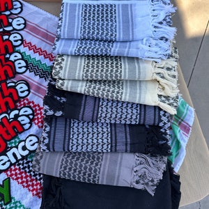 Puede incluir: Una pila de ocho pañuelos con estampado en blanco y negro con flecos. Los pañuelos están doblados y apilados uno encima del otro. El pañuelo superior es blanco con rayas negras y un patrón en blanco y negro. El pañuelo inferior es negro.