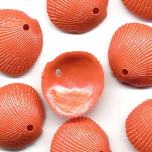 May include: A collection of orange seashell-shaped beads, each featuring a single drilled hole near the top edge. The beads display a detailed, ribbed texture on their exterior surfaces, while one bead is positioned to show its smooth, concave interior.
