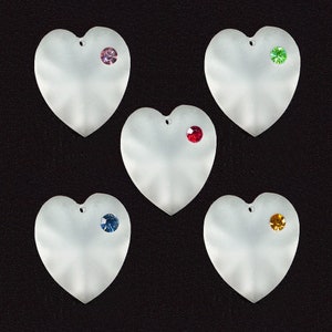 May include: Five white heart-shaped ornaments with different colored rhinestones. The rhinestones are pink, green, red, blue, and yellow.