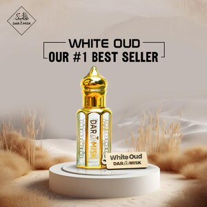 May include: A gold-topped perfume bottle labeled "White Oud" and "DAR MISK" sits on a white pedestal. The bottle is clear with gold accents and a decorative design. The background features text that reads "OUR #1 BEST SELLER".