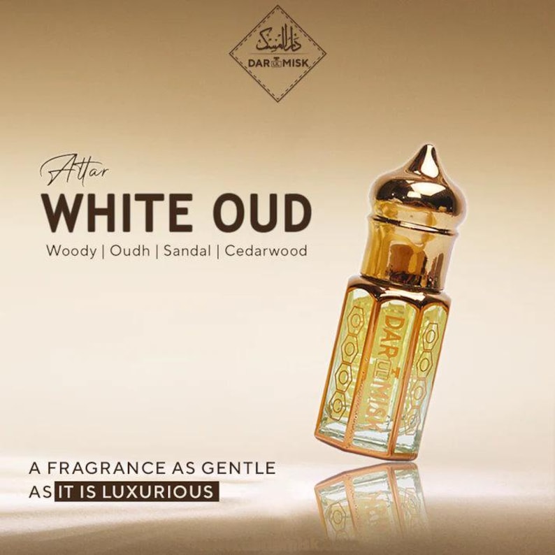May include: A gold-topped perfume bottle with a clear, rectangular body. The bottle is labeled "WHITE OUD" with the words "Woody | Oudh | Sandal | Cedarwood" below. The text "A FRAGRANCE AS GENTLE AS IT IS LUXURIOUS" is also visible.