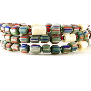 May include: A multi-strand beaded bracelet with green, red, white, and blue beads. The bracelet has two white beads with a carved design and a silver cross charm.