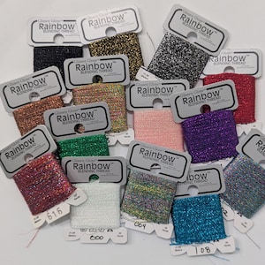 May include: A collection of spools of Glissen Gloss Rainbow Blending Thread in various colors, including black, gold, silver, red, pink, purple, green, and blue. Each spool has a white tag with the brand name and product information.