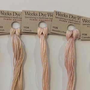 May include: Five skeins of Weeks Dye Works floss in shades of pink, peach, and cream. Each skein is labelled with a number and colour name, including "Saltwater Taffy" and "Meredith's Pink". The floss is presented on a neutral background.