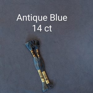 May include: A piece of antique blue 14 ct Aida cross stitch fabric with a visible grid texture, accompanied by two skeins of blue embroidery floss featuring gold paper labels with the text DMC 931 and 930.