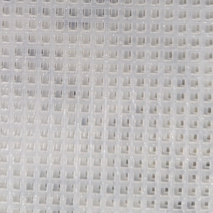 May include: A close-up shot of a white, square-grid fabric. The grid is made up of small, evenly spaced squares. The material appears translucent, with slight variations in light and shadow across the surface.