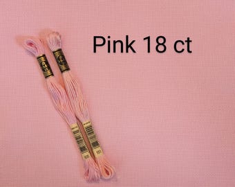 May include: Two skeins of light pink embroidery floss with black and gold paper labels, positioned diagonally over a solid light pink 18 ct Aida fabric background. The text Pink 18 ct is printed in black on the upper right side of the image.