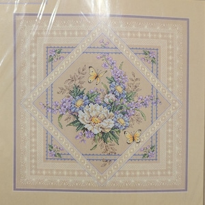 Può includere: Ricamo a punto croce con un bouquet floreale con una grande peonia bianca, fiori lavanda e blu. Sono presenti due farfalle gialle. Il disegno è incorniciato da un bordo beige e lavanda con un motivo a diamante.