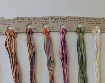 Könnte beinhalten: Eine Präsentation von Weeks Dye Works Garnen, Holiday Collection, in verschiedenen Farben. Das Garn ist an Pappkarten mit dem Namen und der Nummer jeder Farbe befestigt. Zu den Farben gehören Trick or Treat, Harvest, Noel, Confetti, Love, Lucky, Spring Rose und Mother's Day.