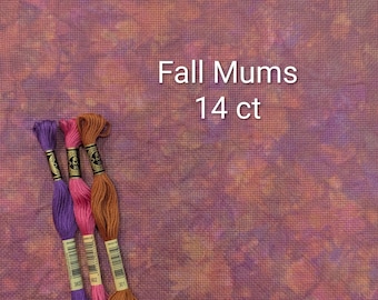 May include: A piece of 14 ct cross stitch fabric with a mottled pattern in shades of purple, orange, and brown, labeled Fall Mums 14 ct. Three skeins of embroidery floss in solid purple, pink, and brown are positioned on the left side of the fabric.