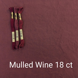 Puede incluir: Tres carretes de hilo de bordar en tonos rojos, etiquetados con los números 3802, 3803 y 3814. El hilo está sobre un fondo de tela rojo oscuro. El texto "Mulled Wine 18 ct" está impreso debajo del hilo.