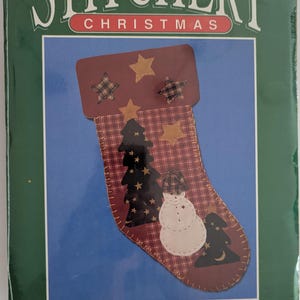 May include: A Christmas stocking kit with the text "STITCHERY CHRISTMAS". The stocking features a burgundy top with plaid stars, a plaid pattern, and appliqued trees and a snowman. The stocking measures 20 cm x 36 cm.