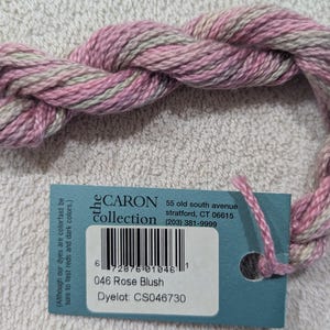 May include: A skein of Caron Collection yarn in Rose Blush, with a label showing the color name, dye lot, and barcode. The yarn is a twisted bundle of pink and gray threads, ideal for knitting or crochet projects.