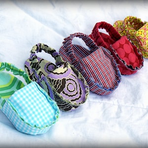 Puede incluir: Una colección de cinco zapatos de bebé coloridos. Los zapatos presentan varios patrones, incluyendo cuadros, florales y lunares, en tonos de azul, verde, rojo y amarillo. Cada zapato tiene una construcción de tela suave con elástico alrededor del tobillo.