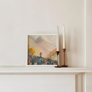 May include: A framed watercolour painting depicting a crowd gathered before a figure on a hill, with mountains in the background. Two white candles stand in brass candle holders on a white shelf.