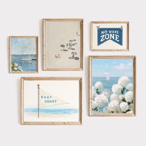 May include: A collection of framed coastal art prints. The prints feature beach scenes, sailboats, and floral elements in soft blues, whites, and beige tones. One print displays the text "NO WAKE ZONE" on a blue banner.