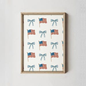 May include: Framed print featuring a repeating pattern of American flags and blue bows on a white background. The flags are red, white, and blue, and the bows are a soft blue. The frame is a light, neutral color.