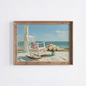Könnte beinhalten: Gerahmtes Gemälde mit einem weißen Schaukelstuhl mit einem Kissen mit der amerikanischen Flagge auf einer Holzveranda. Eine blaue Vase mit rosa und weißen Blumen ist ebenfalls zu sehen. Das Kunstwerk ist in einem hellbraunen Holzrahmen gerahmt.