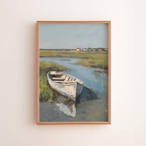 Könnte beinhalten: Gerahmtes Landschaftsgemälde mit einem weißen Ruderboot am Rande eines blauen Wasserwegs. Das Boot liegt in der Nähe von grünem Marschgras, mit einer fernen Küstenlinie mit kleinen Gebäuden unter einem blassblauen Himmel. Das Kunstwerk ist in einem Holzrahmen.
