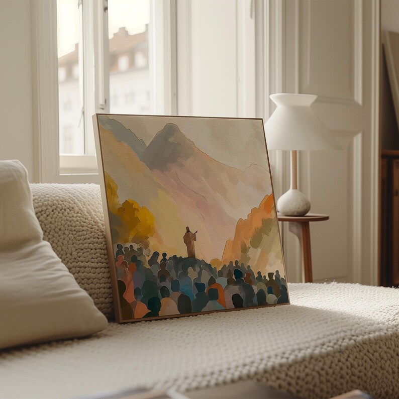 May include: A framed watercolour painting shows a figure addressing a crowd on a hill, with mountains in the background. The artwork uses warm colours like orange, yellow, and blue. The painting is displayed on a beige sofa.