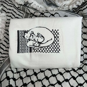 May include: White embroidered tote bag featuring a black and white illustration of two cats cuddling. The illustration is surrounded by a black and white geometric pattern.