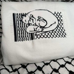 May include: White sweatshirt featuring a black embroidered design of two cats cuddling inside a fence. The design is in a vintage style.