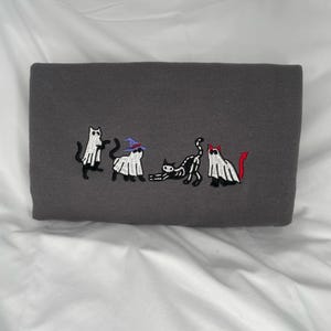 May include: A gray sweatshirt with an embroidered design of five cats dressed as ghosts for Halloween. One cat is wearing a witch's hat, another has a devil's tail, and the other three are wearing simple ghost costumes.