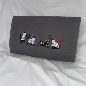May include: A gray sweatshirt with an embroidered design of five cats dressed as ghosts for Halloween. One cat wears a witch's hat, another has a devil's tail, and the others are plain ghosts.