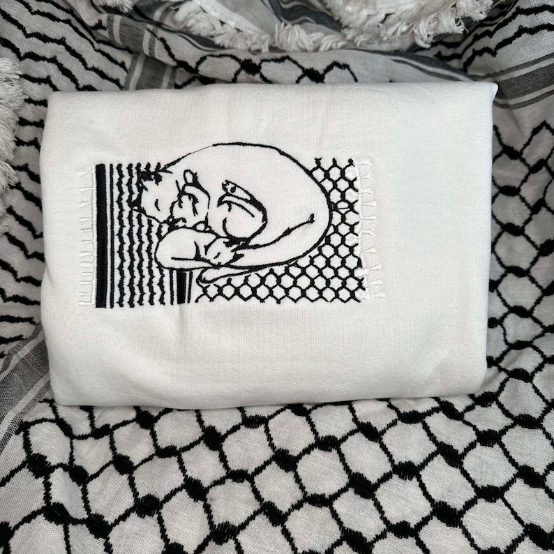 May include: White t-shirt featuring a black embroidered design of two cats cuddling. The design is framed by a black and white geometric pattern.