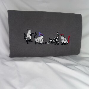 May include: A gray sweatshirt with an embroidered design of five cats dressed as ghosts for Halloween. The cats are wearing witch hats, devil horns, and ghost costumes.