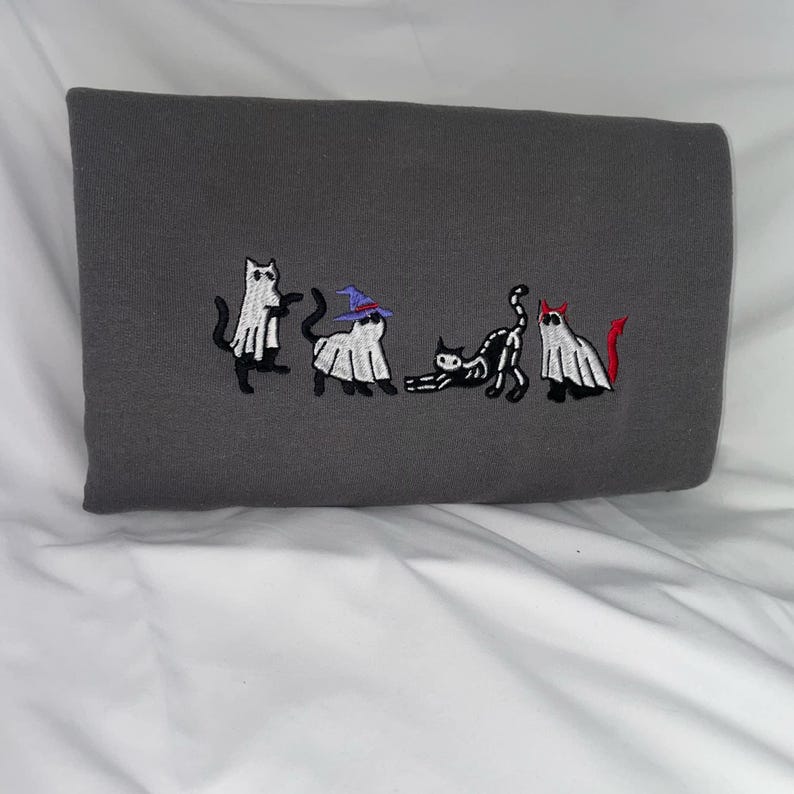 May include: A gray sweatshirt with an embroidered design of five cats dressed as ghosts for Halloween. The cats are wearing witch hats, devil horns, and ghost costumes.