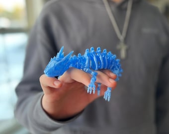Puede incluir: Un esqueleto articulado de lagarto o dragón de plástico azul. El esqueleto está en posición con la cabeza levantada y las patas extendidas.