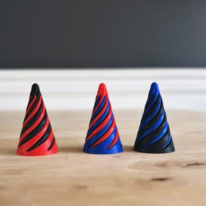 May include: Three decorative cones with a spiral pattern. The cones are red, blue, and black.