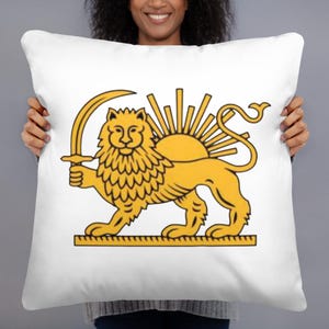 May include: White throw pillow featuring a golden lion holding a sword, with a sunburst design in the background. The lion is standing on a golden rectangular base. The design is centered on the pillow.