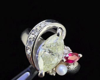Op de afbeelding: Een zilveren ring met een grote, lichtgroene, peervormige edelsteen. De ring is versierd met een kleinere rode edelsteen, een witte parel en kleine heldere stenen. De band is versierd met kleine, heldere stenen.