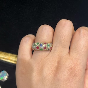 May include: A wide gold band ring featuring a pavé setting of round-cut gemstones. The surface is densely encrusted with small, clear white diamonds interspersed with larger, vibrant round-cut rubies, emeralds, and blue sapphires in a multi-colored pattern.