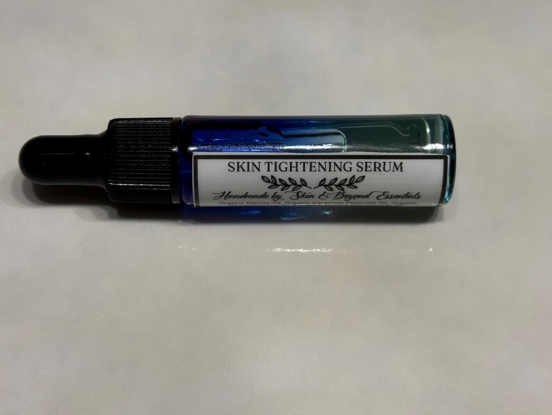 Pu&ograve; includere: Un piccolo flacone di vetro blu con un contagocce e un'etichetta bianca che recita "SKIN TIGHTENING SERUM Handmade by Skin & Beyond Essentials".